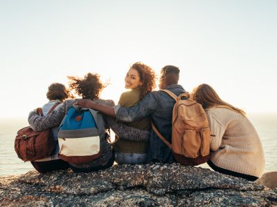 Werde kreativ und überzeuge uns von deiner Neugier! Junge Menschen von hinten fotografiert, eine junge Frau blickt lachend in die Kamera