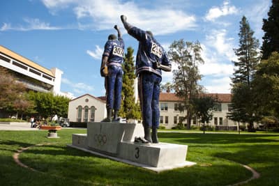 Statue von Tommi Smith und John Carlos auf dem Campus der SJSU Olympisches Podest mit zwei Sportlern auf grüner Wiese