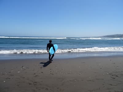 Die Surfstrände nahe der UVM bieten gerade für Anfänger perfekte Bedingungen. Surfer mit Surfboard in Chile.