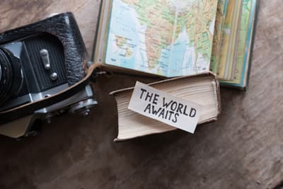 Nach der langen Schulzeit erst einmal die Welt entdecken! Karte, Fotoapparat und ein Schild "The World Awaits"