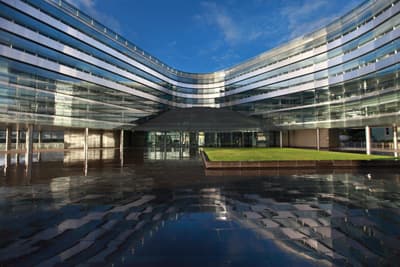 Kontrastreich: Auf dem City Campus der Uni treffen historische Gebäude auf futuristische! Ein geschwungenes, gläsernes Gebäude und dessen Reflexion auf dem nassen Boden