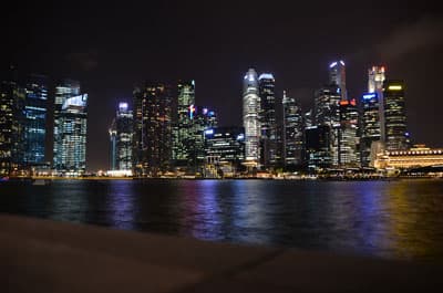 Mehrere Hochhäuser hinter einem nächtlichen Hafen Die Sykline von Singapur