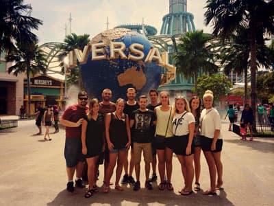 Die Universal Studios auf Sentosa Eine Gruppe junger Menschen vor dem Universal Studio Emblem