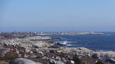 Die Atlantikküste in Nova Scotia Eine steinige Meeresküste mit Häusern und einem Leuchtturm im Hintergrund