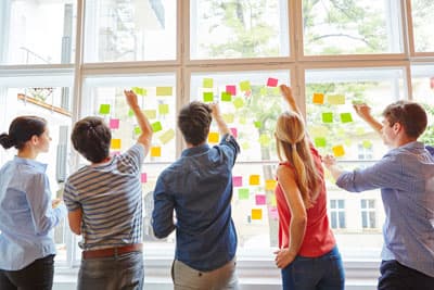 In jedem steckt Kreativität - schöpft sie in Design Thinking Kursen aus. Studierende kleben postiITs ans Fenster