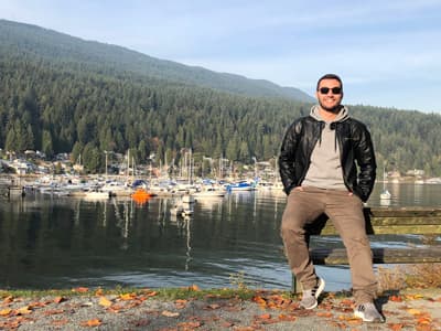 Abschalten Marvin lehnt an einer Bank. Hinter ihm sieht man zahlreiche Boote und typisch kanadische Natur mit bewaldeten Hügeln.