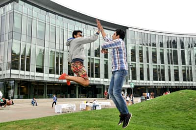 Der TRU-Community-Spirit Zwei internationale Studenten geben sich High-Five während eines Luftsprungs auf dem Campus der TRU