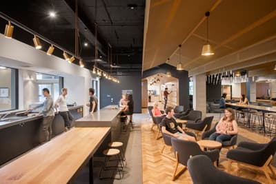 Eine Lounge mit Holztischen, Hockern und Stoffsesseln