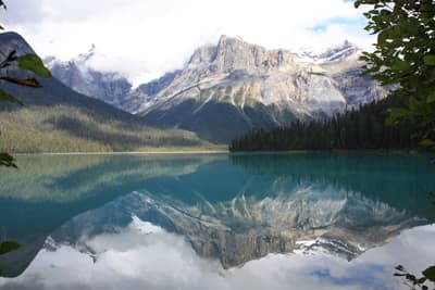 Entdecke die kanadischen Rockies! Eine Berglandschaft spiegelt sich in einem strahlend türkisblauen Gletschersee