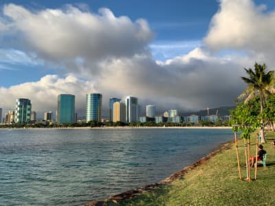 Am Meer gebaut Blick von einer grünen Uferpromenade über das Wasser auf die Skyline von Honolulu