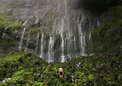 So viel zu entdecken! Student vor einem sehr hohen, verzweigten Wasserfall, der über bemooste Felsen hinabfällt