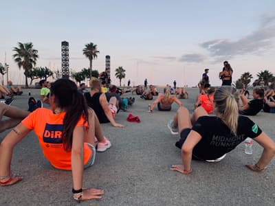 Immer in Bewegung bleiben! Dynamisches Bild einer Laufgruppe, die in der Nähe des Strandes Aufwärmübungen im Freien bei Abendstimmung macht