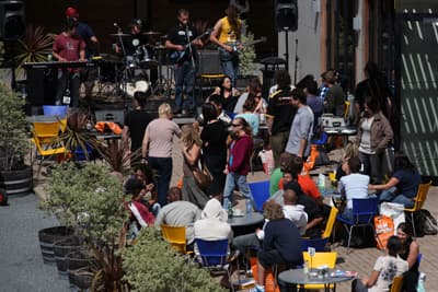 Ganz entspannt Gut besuchte Caféterasse, auf der Menschen in der Sonne sitzen, im Hintergrund spielt eine Band Livemusik