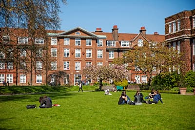 Studenten auf einer mit Bäumen besäten Wiese vor dem Campusgebäude.