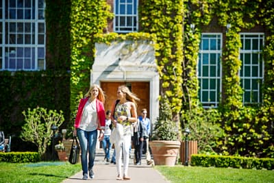Studienerlebnis der Extraklasse Zwei Studentinnen kommen aus einem efeubewachsenen Ziegelstein-Gebäude der Regent's University