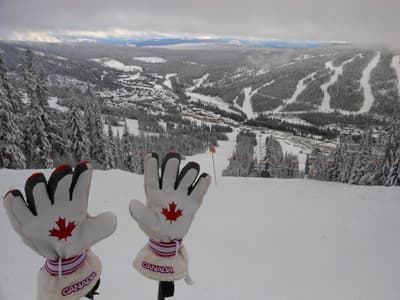Kanadas zweitgrößtes Skigebiet ist nur einen Katzensprung entfernt Schneehandschuhe mit kanadischem Ahornblatt vor dem Panorama der verschiedenen Abfahrten des Sun Peaks Skigebiets
