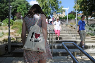 Studentin spaziert mit einer Tasche der University of Bristol. Studentin an der University of Bristol spaziert auf dem Gehweg.