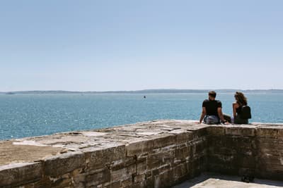 In Portsmouth erwartet dich ein tolles Gesamtpaket Zwei Studierende sitzen auf einer Mauer in Old Portsmouth und schauen aufs Meer hinaus.