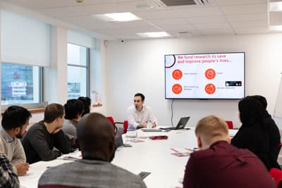 Unternehmensberatung hautnah erleben - die Business Clinic macht's möglich! Studierende sitzen um einen Tisch in der Business Clinic und diskutieren mit einem Dozierenden.