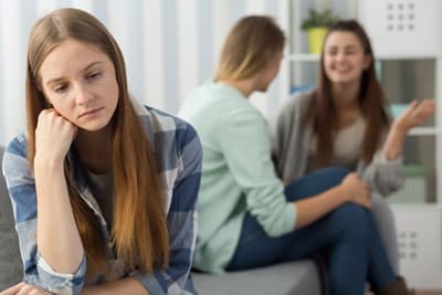 Chronische Krankheiten müssen kein Hinderungsgrund für ein Auslandsstudium sein. Eine Studentin sitzt abseits und schaut traurig nach unten.